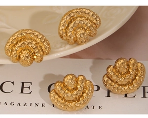 Detail of vintage gold fan-shaped earrings with hammered texture on a ceramic tray