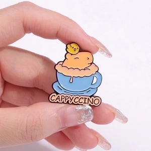 Enamel capybara Cappyccino pin with a chick in a blue coffee cup held by fingers
