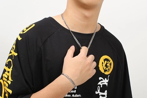 Detail of a silver cuban link chain necklace and bracelet set worn by a male model