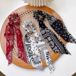 Set of three paisley printed silk hair scrunchies in red, white and black on a tray