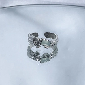 Close-up of irregular silver ring with square green gemstone on a reflective surface