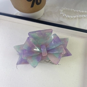 Detail of purple and green gradient bow hair claw with glitter finish on a white box