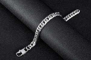 Macro view of silver cuban chain bracelet with secure lobster clasp on black texture