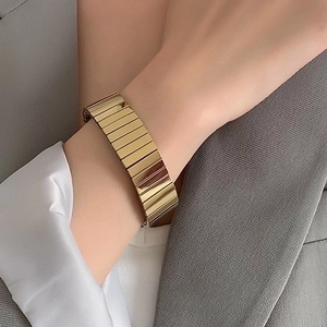 Close-up of a wide gold ribbed link bracelet worn with a professional grey business suit