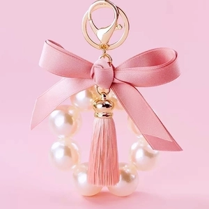 Cute pink satin bow keychain with white pearls and tassel on a golden metal ring