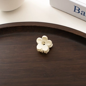 Close-up of a white mini floral hair clip on a vintage dark wooden tray with aesthetic decor
