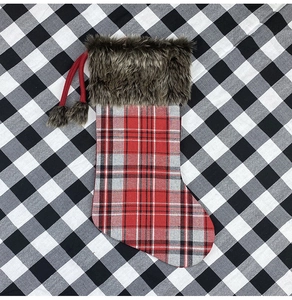 Detail of a plaid Christmas stocking with brown faux fur trim and red pompom drawstrings