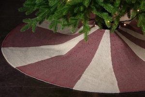 Detailed knit texture of red and beige striped Christmas tree skirt under warm festive lights