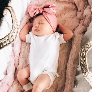 Pink cashmere baby turban with large bow shown on a newborn in a cozy woven basket
