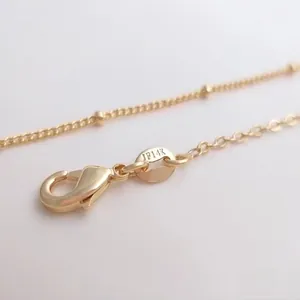Macro shot of 14K gold plated necklace featuring a lobster clasp and satellite chain detail