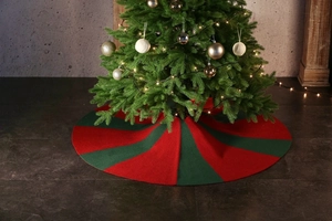 Detail of red and green striped knitted Christmas tree skirt on dark textured floor