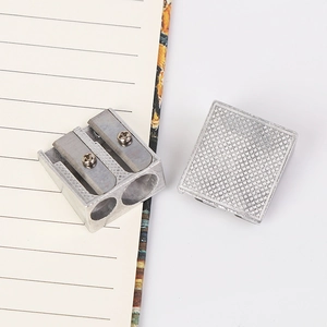 Dual-hole silver aluminum pencil sharpener with textured cap on notebook background