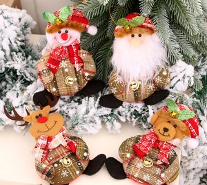 Close-up of plush Christmas bell ornaments including Santa and Reindeer on pine branches