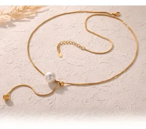 Detail einer goldenen Schlangenkette mit großer weißer Muschelperle und Goldkugel-Anhänger