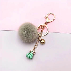 Detail of gray faux fur pompom keychain with gold chain and mint green leather tassel