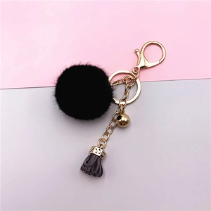 Detail of creative keychain with black faux fur pom pom and dark grey suede tassel charm