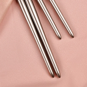 Détail de quatre manches de pinceaux à maquillage dorés sur un tissu en satin rose