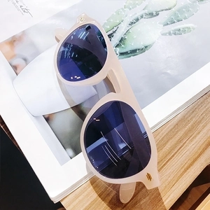 Stylish cream-colored square sunglasses with dark blue lenses on a magazine backdrop