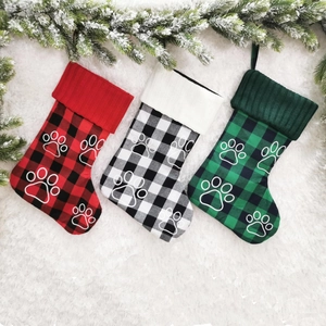 Close-up of three plaid Christmas stockings with white paw embroidery on snowy background