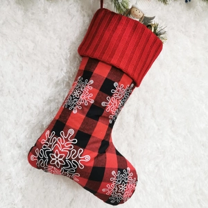 Detail of red and black plaid Christmas stocking with white snowflake prints on plush background