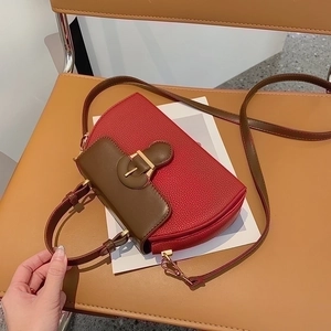 Detail of red and brown saddle handbag featuring vintage gold buckle and pebble leather