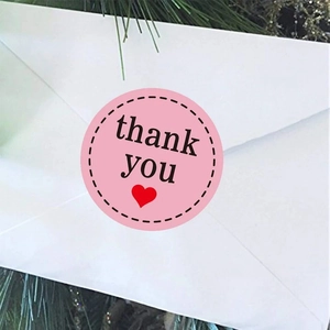 Close-up of pink round thank you sticker with red heart on a white envelope