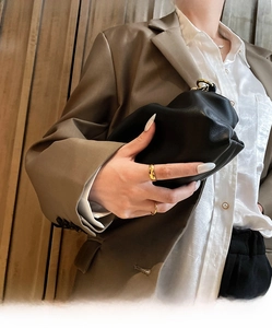 Chic black pleated leather clutch bag held by model wearing a stylish brown blazer