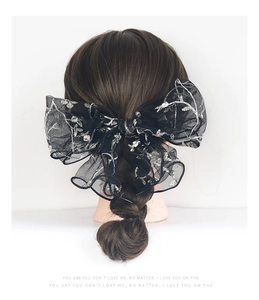 Detail of a large black mesh bow hair clip with silver floral embroidery on a braided hairstyle