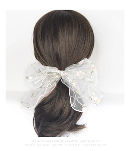 Detailed view of white mesh bow hair clip with pink and green floral embroidery