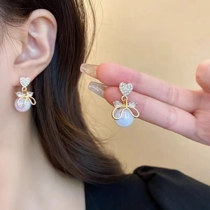 Detail of heart stud earrings with golden bows and lustrous faux pearls for women