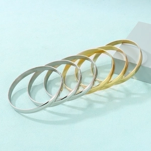 Detail showing gold and silver stacked 8mm stainless steel bracelets on light blue texture