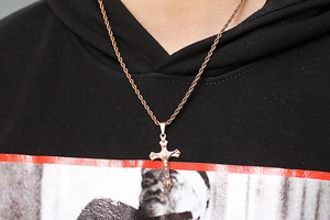 Detail of rose gold crucifix pendant on a rope chain worn by a model in a hoodie
