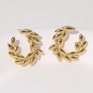 Macro shot of gold laurel leaf stud earrings in stainless steel on white background
