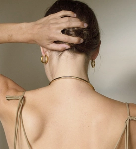 Detailed close-up of a model wearing minimalist golden C-shaped hoop earrings and choker
