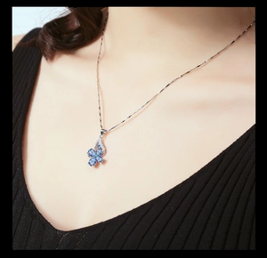 Close-up of a silver four-leaf clover pendant with blue topaz stones on a model's neck