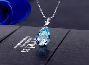 Macro shot of a teardrop blue crystal pendant with a silver box chain on a gift box