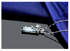 Macro shot of silver rhombic necklace with a blue gemstone on a dark fabric background