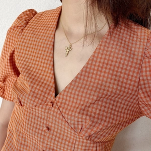 Close-up of a mini gold angel pendant necklace worn with a stylish orange plaid dress