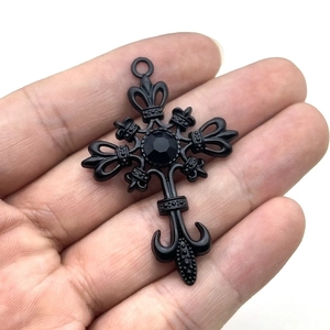 Gothic punk cross pendant with black gemstone shown in palm for size reference