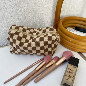 Brown checkered knit makeup bag on a desk with cosmetics and makeup brushes