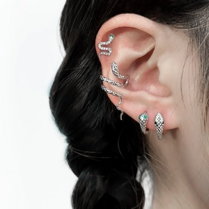 Detailed close-up of silver snake earring set featuring green eye accents on a model ear