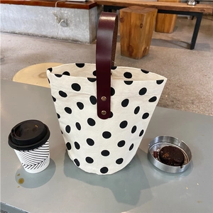 Detailed view of canvas bucket bag with black polka dots and a red leather handle