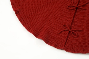 Detailed macro shot of red knitted Christmas tree skirt featuring cozy tie-bow decorations