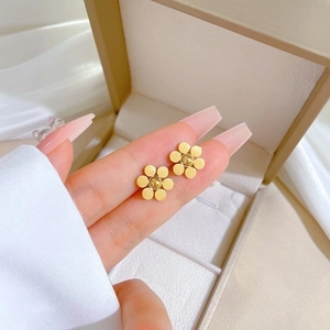 Minimalist matte gold six-petal flower stud earrings held by a hand for scale