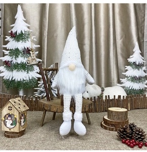 Detail of white plush Christmas gnome with sequined hat and festive wooden cabin props