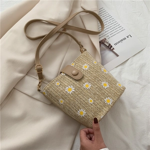 Detail of khaki straw bucket bag with white daisy patterns on a beige blazer