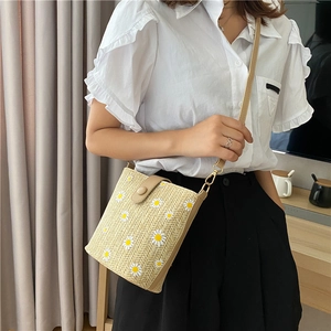 Detail of straw bucket bag with white daisy print and slim shoulder strap