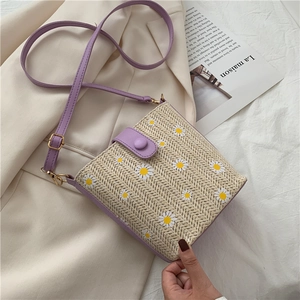 Detail of purple leather trim and daisy pattern on a straw woven crossbody bucket bag