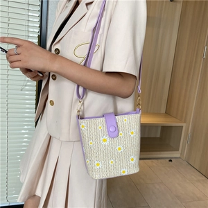 Detail of a beige straw bucket bag with purple PU strap and white daisy print detail