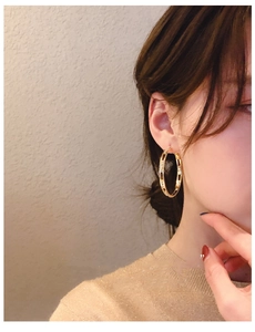 Close-up of model wearing gold hollow circular hoop earrings with sparkling texture